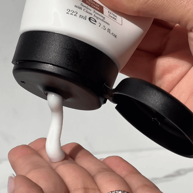 Hand holding a pump bottle with white cream being dispensed onto another hand against a neutral background